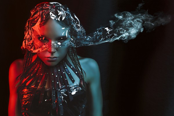 Young woman with black eyes staring at the camera wearing a leather choker necklace and a plastic helmet emitting smoke in front of a black background by Artmood Visualz